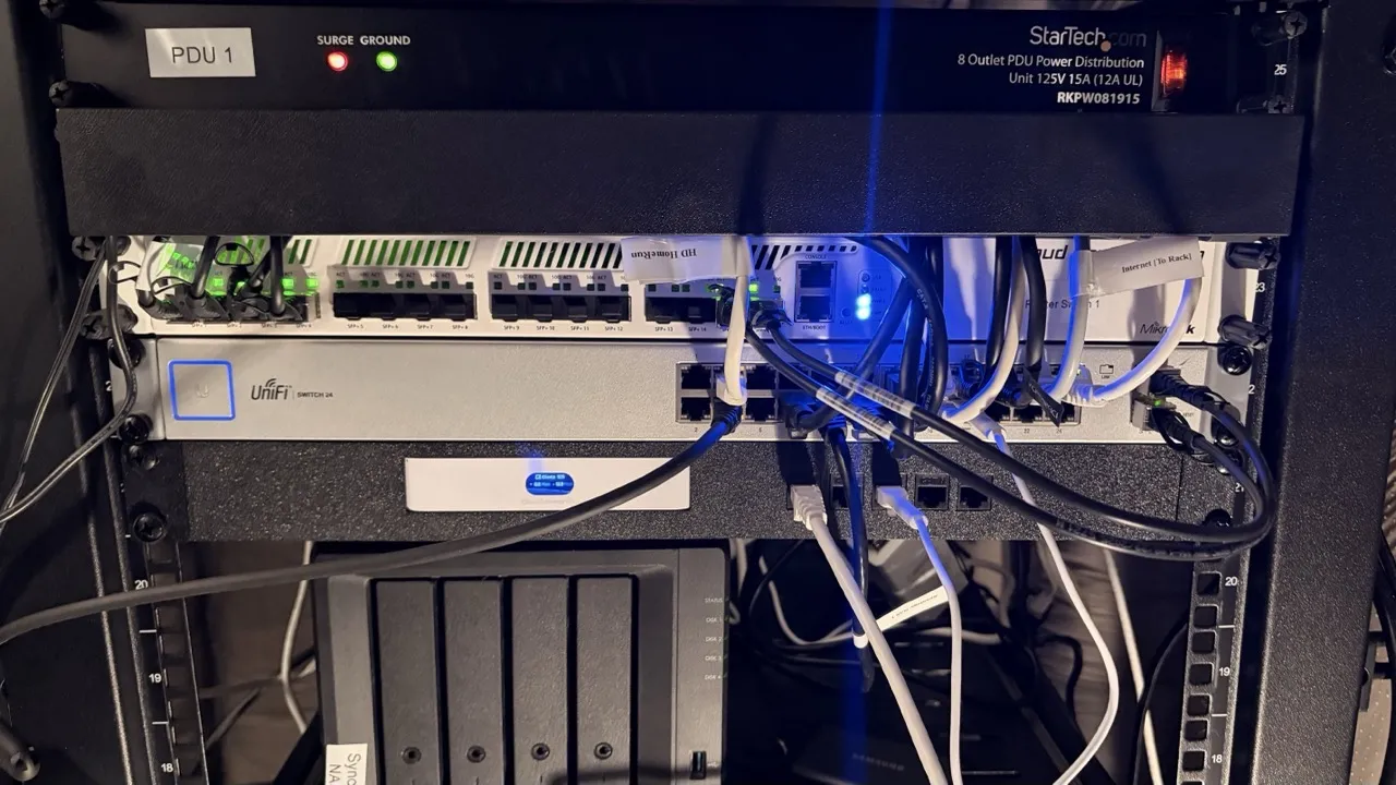 Close-up of the rack top section showing PDU, patch panel, UniFi switch, and Synology NAS with networking cables