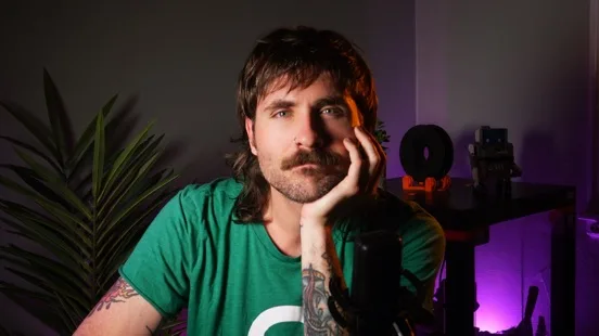 What the camera sees in the recording studio: Joe in a green t-shirt in front of a palm plant and a shelf lit with purple ambient light